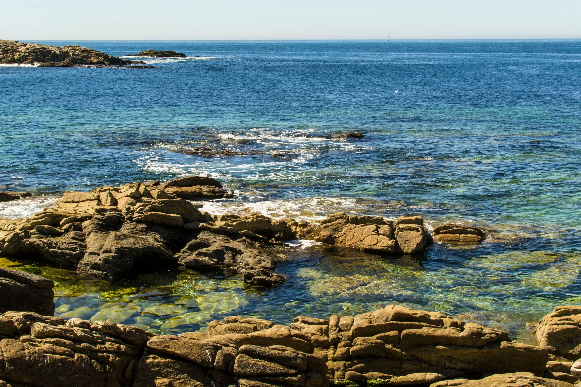 Clear shallow water over sandstone ledges and a reef line along a rocky coast
